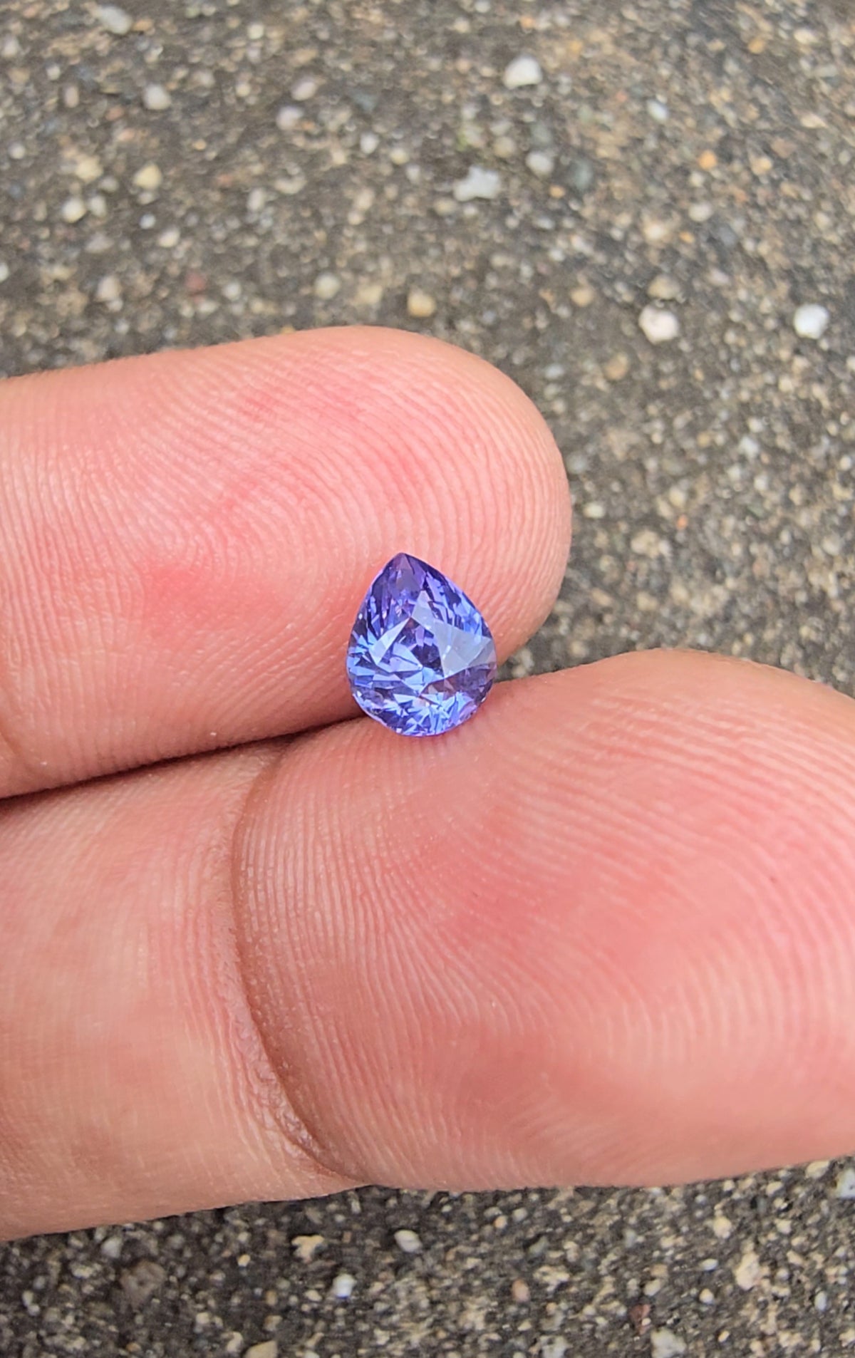 Upright lavender violet pear-cut sapphire resting between fingertips