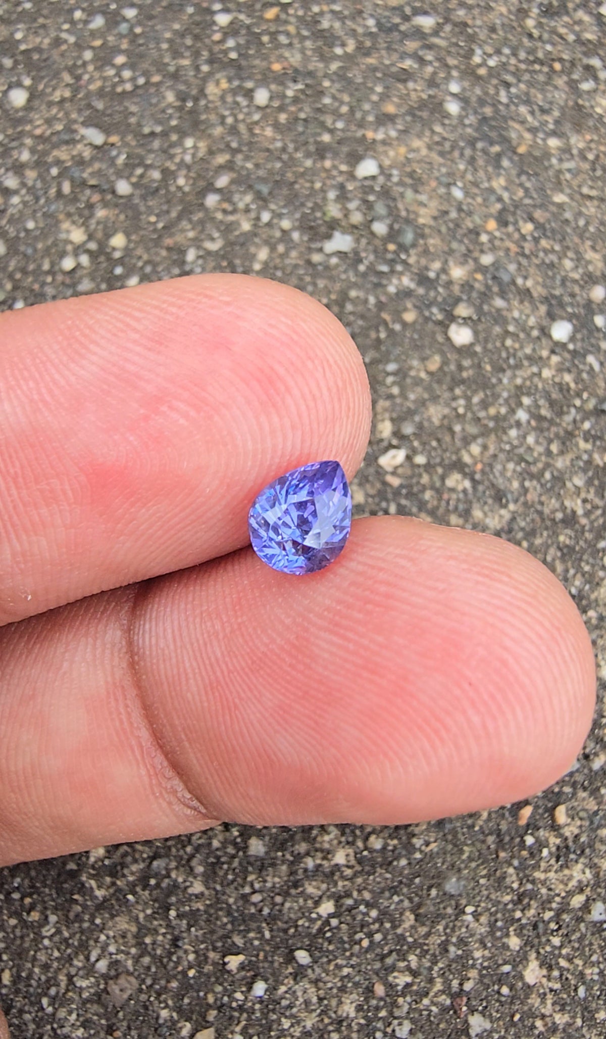 Violet pear-cut sapphire on fingertips showing bright lavender reflections