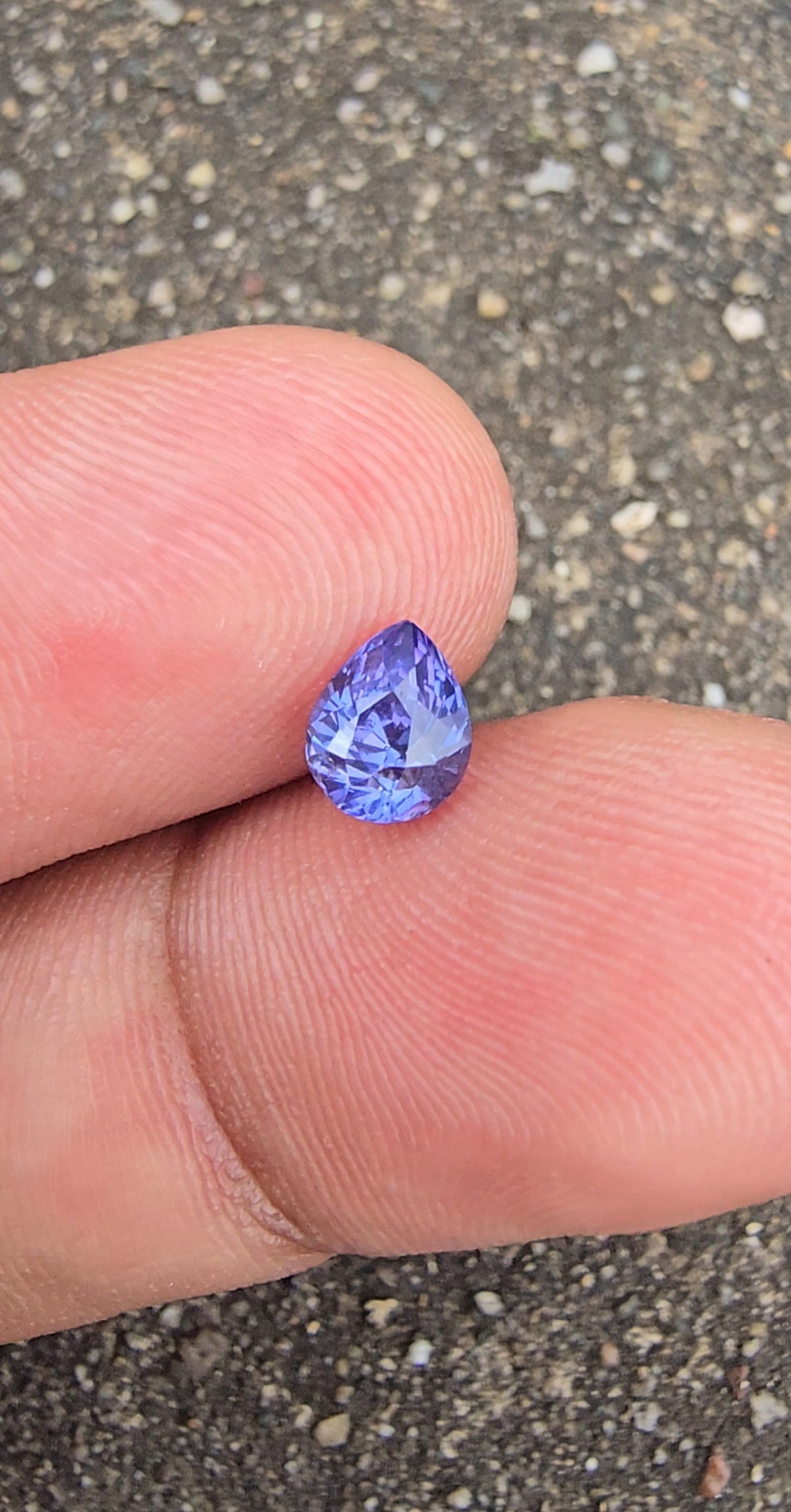 Natural violet pear-cut sapphire resting upright on fingertips
